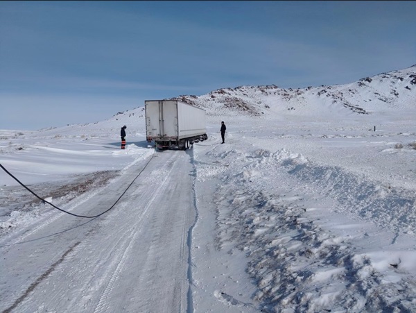 Truck stuck in the snow with two men and a tow strap helping