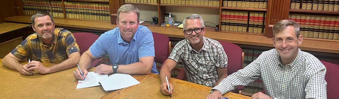 A group signs a contract and smiles at the camera